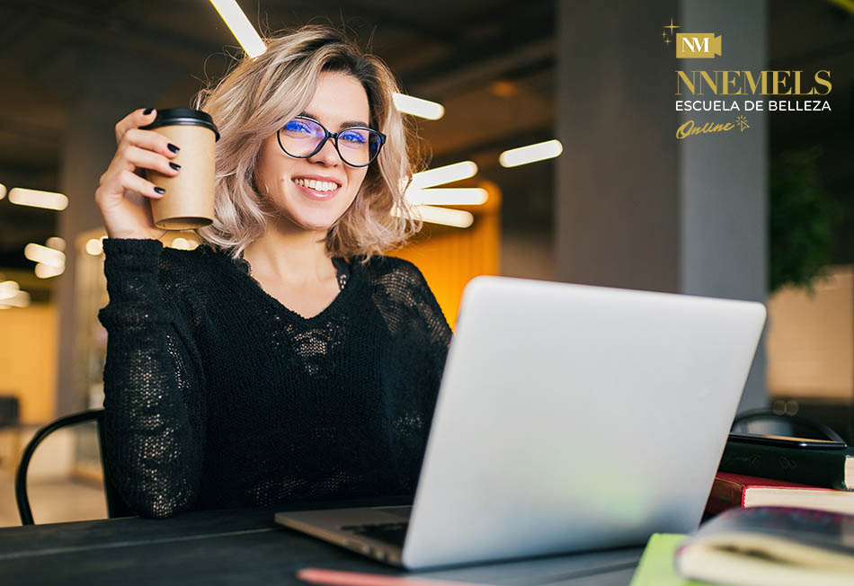 portrait of young pretty woman sitting at table in black shirt working on laptop in co-working office, wearing glasses, smiling, happy, positive, drinking coffee in paper cup
